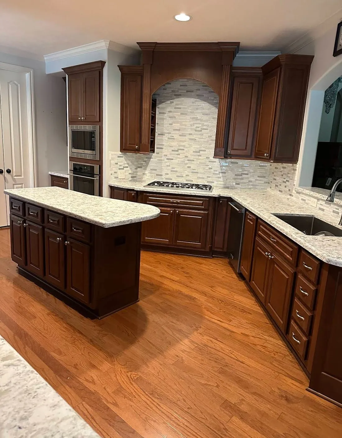 Kitchen before painting, dark cherry raised-panel cabinets and a matching island under a tiled cooking arch, with speckled granite counters