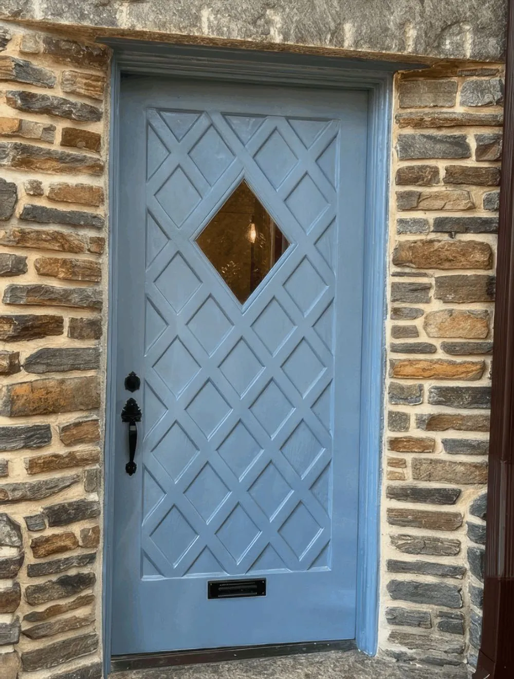 Blue-gray diamond-lattice front door and jamb refinished, set in a fieldstone surround