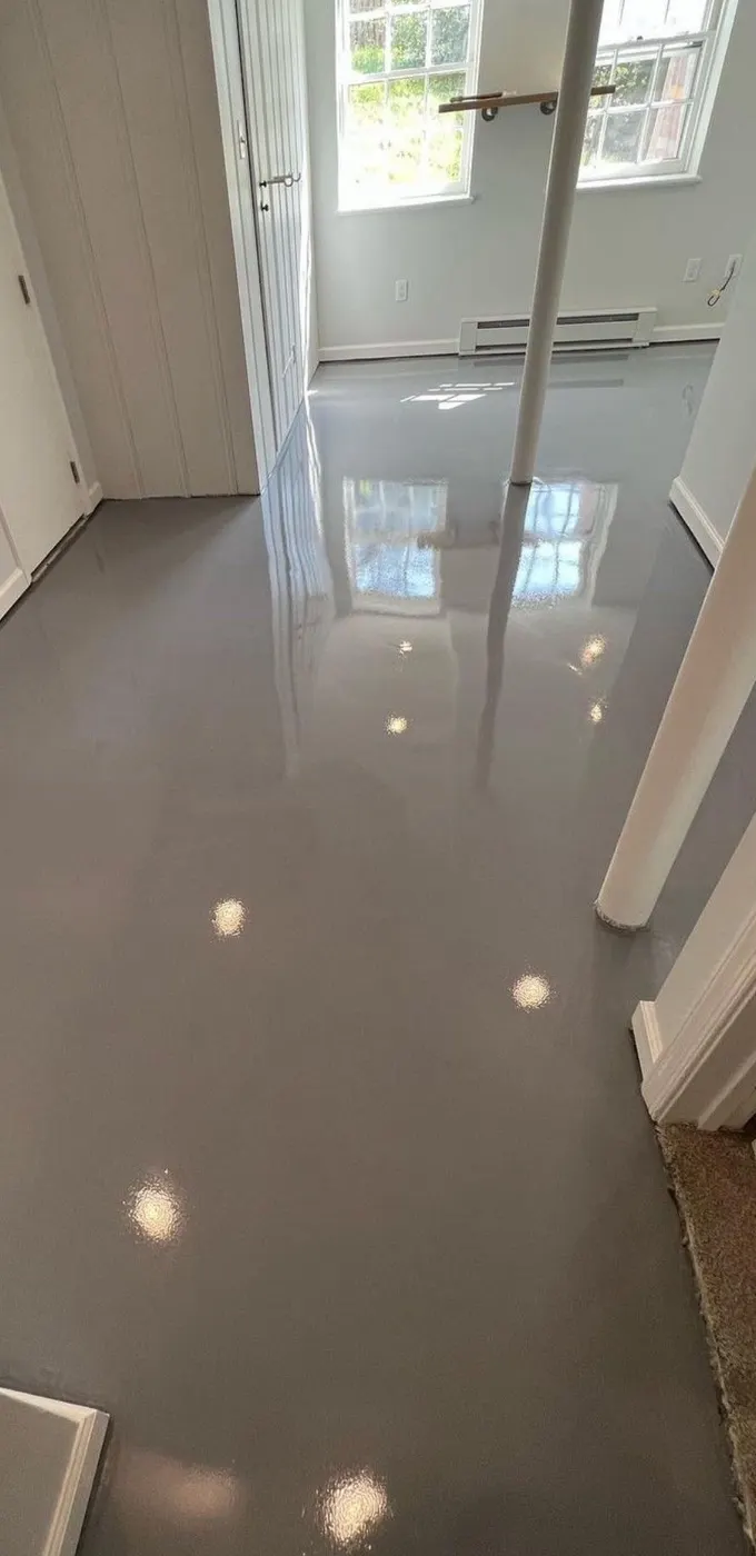 The same basement floor after coating, a smooth high-gloss gray surface reflecting the window light