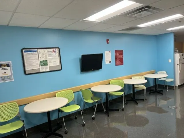 Office break room with a bright blue feature wall above white round tables and green chairs