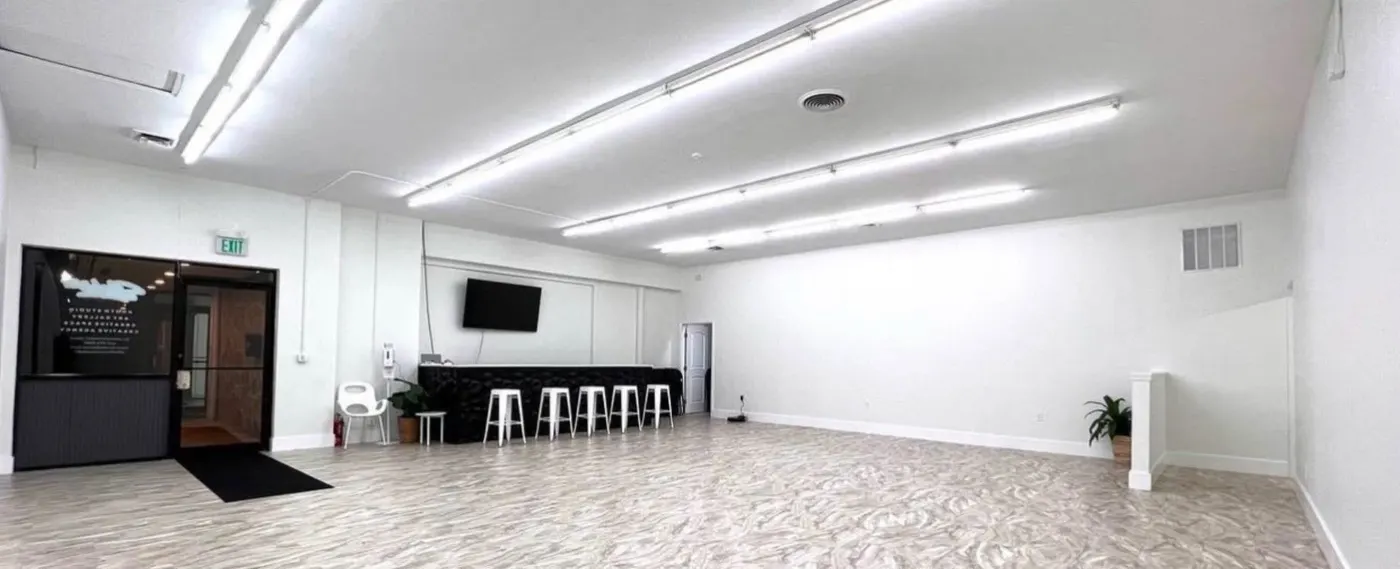 The same commercial room after the repaint, all-white walls and ceiling over a light floor, a black bar with white stools at the far end