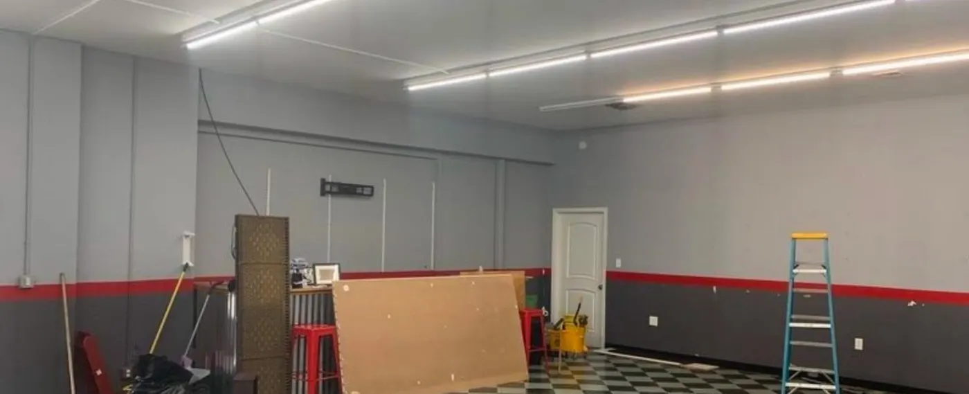 Commercial room before the repaint, gray walls with a red and dark gray band, black and white checkered floor, a ladder and plywood sheets against the wall