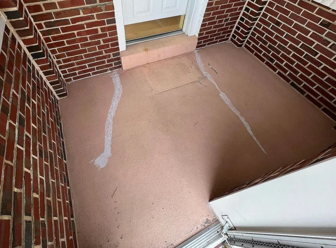 Small entry floor before coating between two red brick walls, the old tan surface scuffed and streaked