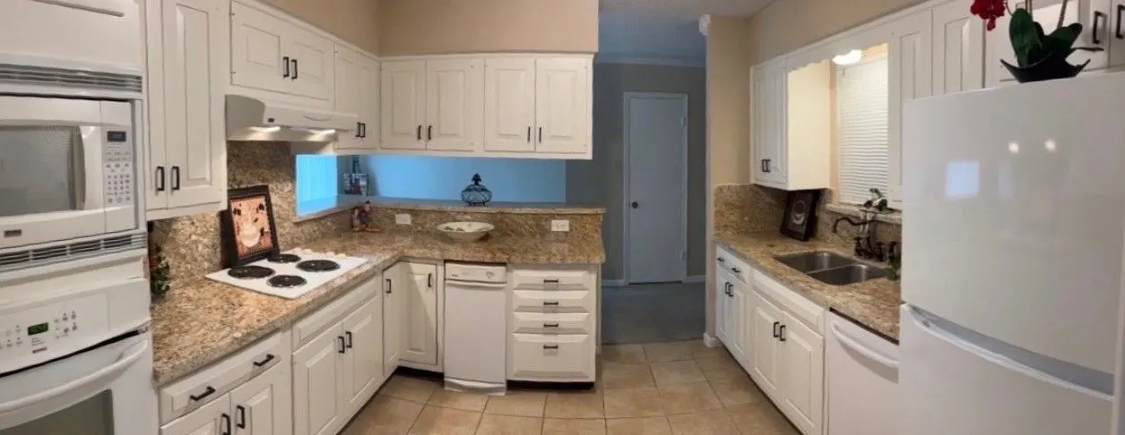 The same galley kitchen after the cabinets were painted white, the granite counters, white appliances and blue backsplash strip unchanged