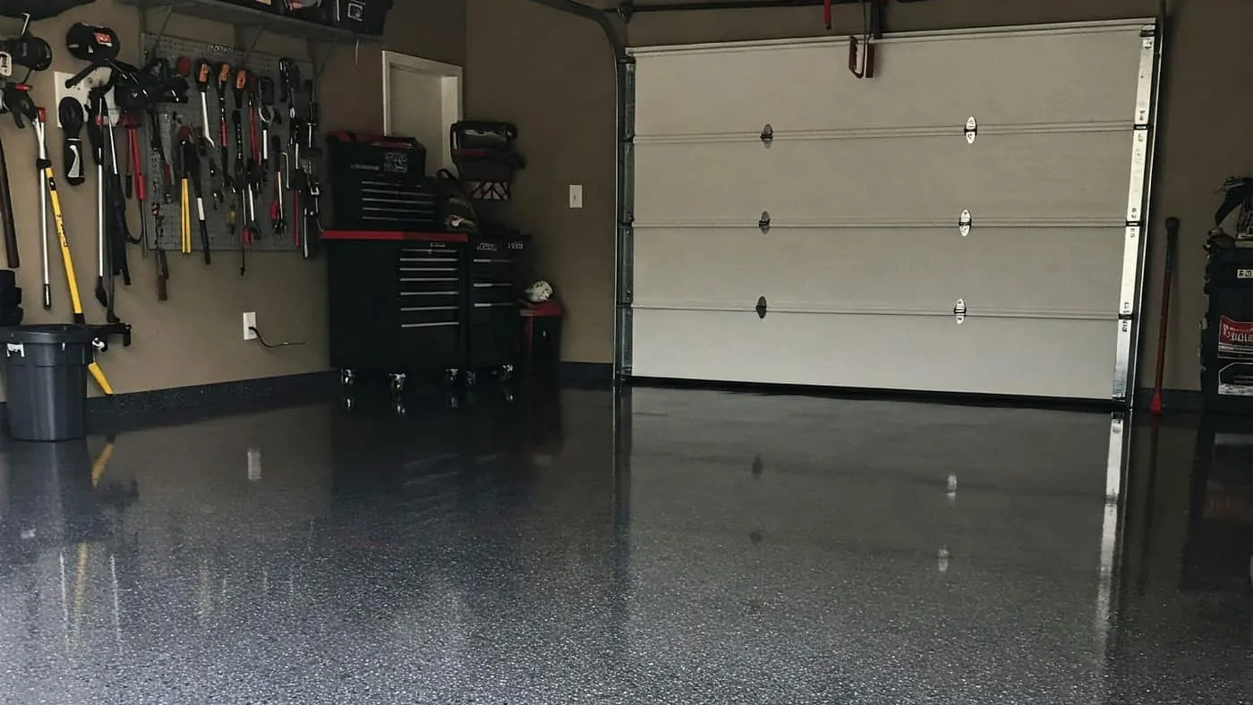 Garage floor finished in a gray and black flake coating, a tool wall and a white roll-up door