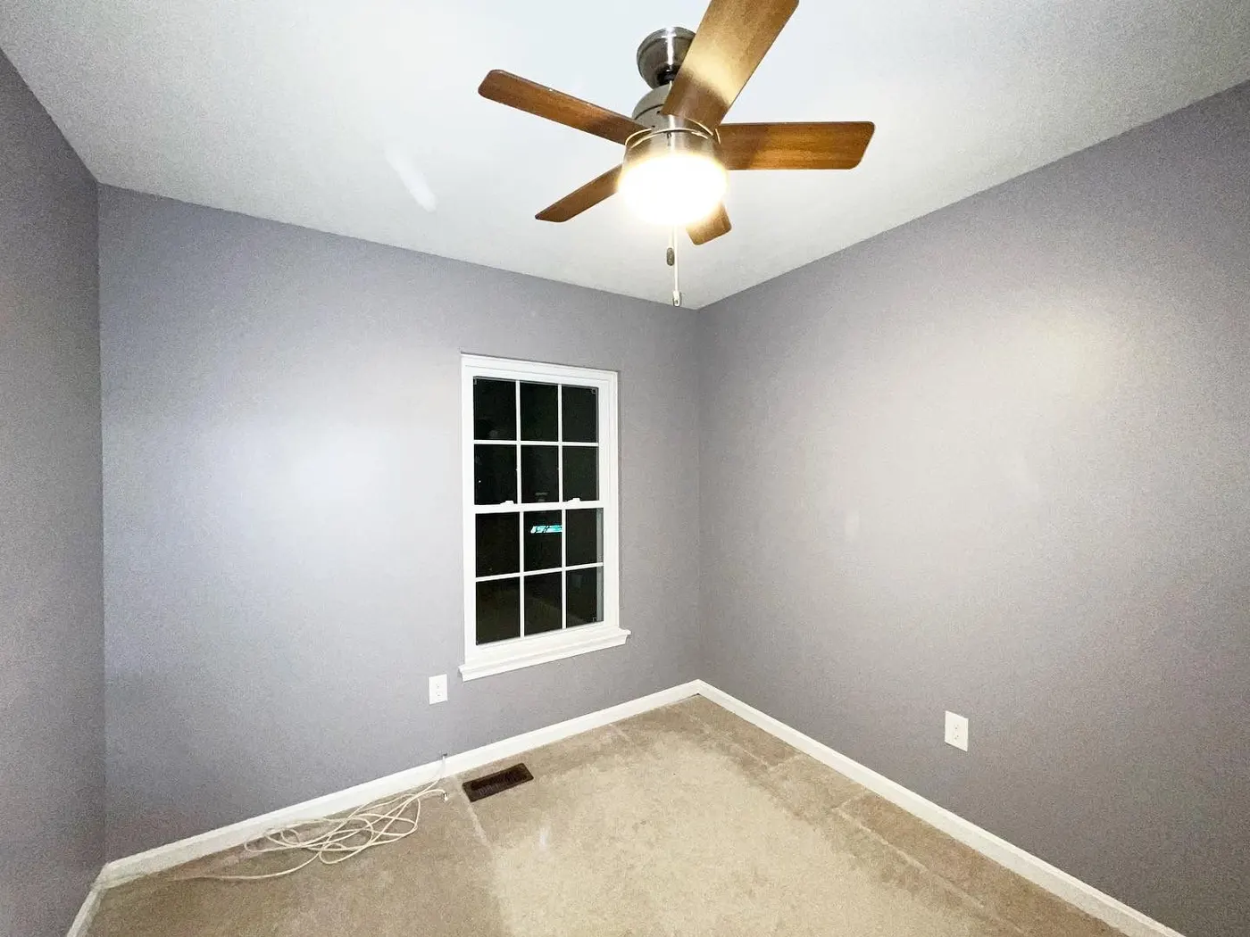 Empty bedroom freshly painted gray with white window trim and baseboards and a ceiling fan