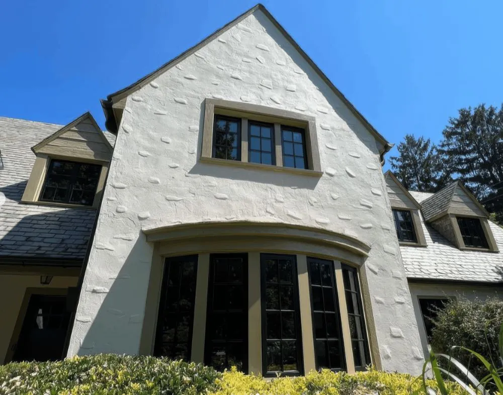 Gable end of a stucco home repainted off-white with tan window trim by Rise and Prime Painting, bay window below