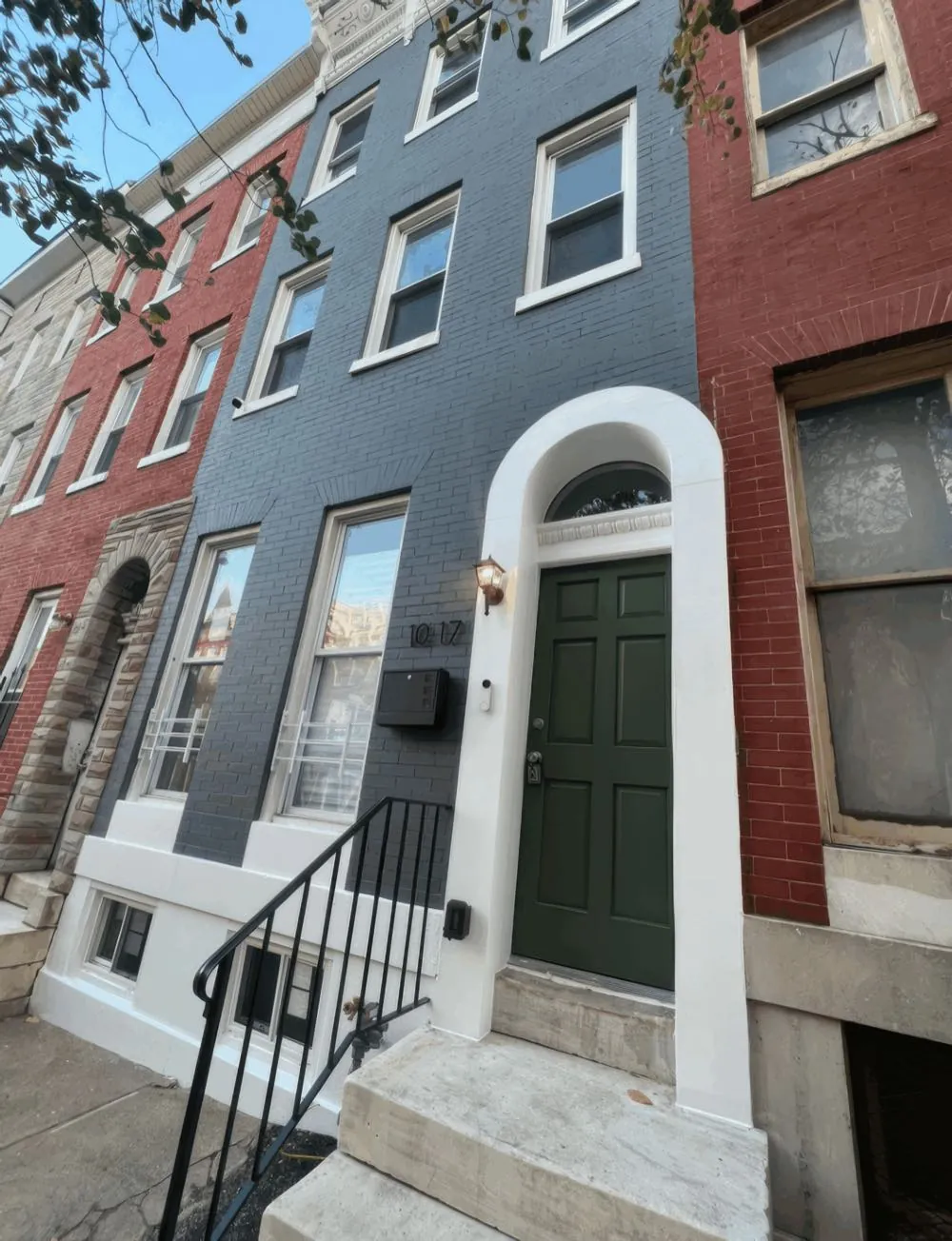 Brick rowhouse front painted slate blue with white window trim, a cream water table and a dark green front door, by Rise and Prime Painting