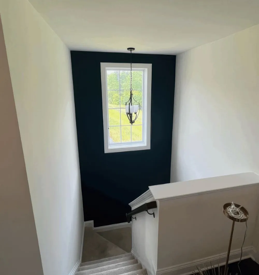 Stairwell landing painted by Rise and Prime Painting with a deep navy accent wall behind the window and white walls, ceiling and trim around it