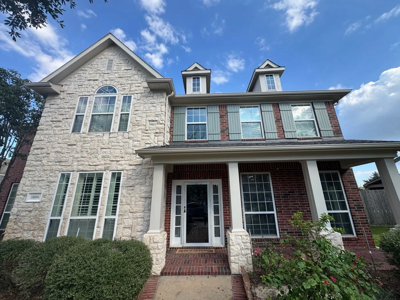 Front of a two-story brick and stone house with white porch columns, dormers and painted shutters, after an exterior repaint by Rise and Prime Painting