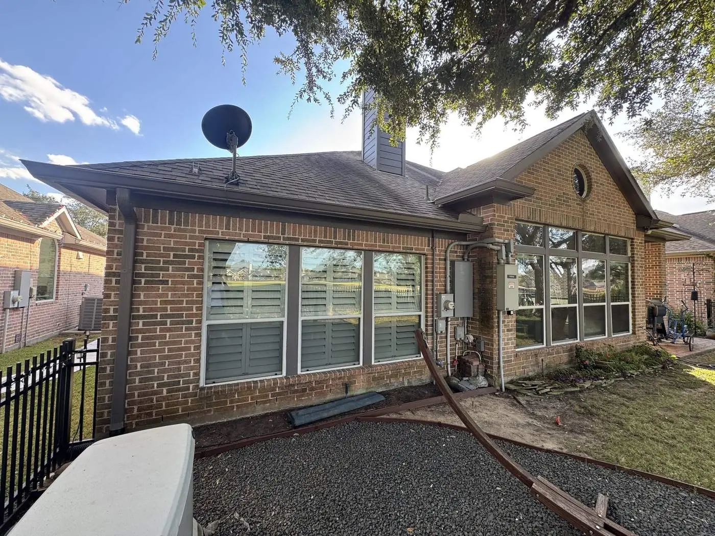 Rear elevation of a red brick home after the eaves and gable trim were repainted, plantation shutters in the windows and a gravel bed along the foundation